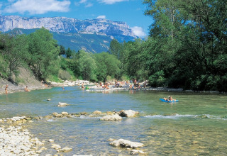 People enjoy the river at Flower Camping la Pinède, with scenic mountains in Auvergne-Rhône-Alpes, France.