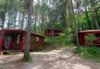 Chalets en bois avec accents rouges dans la forêt au Flower Camping la Pinède, Auvergne-Rhône-Alpes, France.