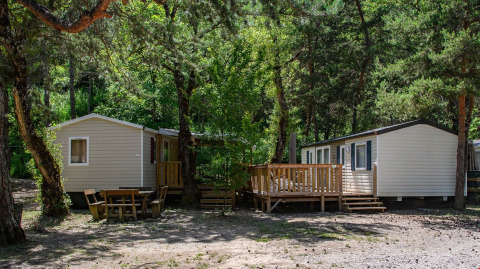 To mobilehomes blandt træer på Flower Camping la Pinède i Auvergne-Rhône-Alpes, Frankrig, omgivet af skov.