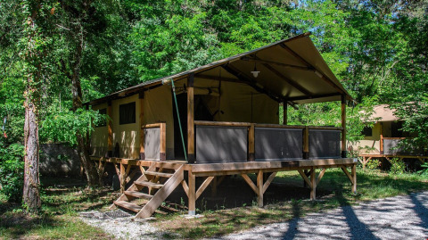 Safari tent cabin at Flower Camping la Pinède surrounded by lush trees in Auvergne-Rhône-Alpes, France.
