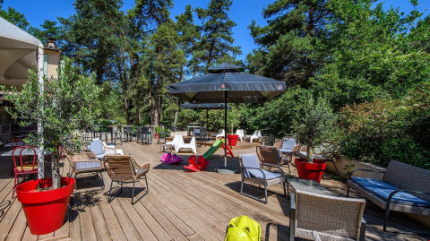 Terrazza esterna a Flower Camping la Pinède con sedute, giochi e alberi in Auvergne-Rhône-Alpes.