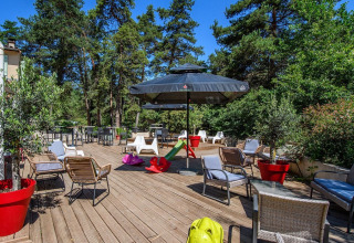 Terrasse extérieure de Flower Camping la Pinède avec sièges, jouets et arbres en Auvergne-Rhône-Alpes.