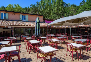 Terrazza esterna con tavoli e sedie al Flower Camping la Pinède, Auvergne-Rhône-Alpes, Francia.