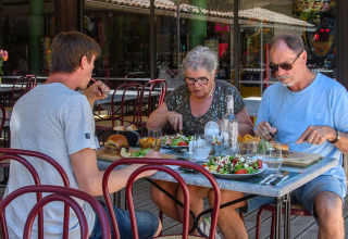 Tre personer nyder et måltid udendørs på en restaurant ved Flower Camping la Pinède i Auvergne-Rhône-Alpes.