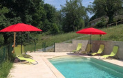 Outdoor pool at Domaine Le Faulion with red umbrellas, green lounge chairs, and lush greenery around.