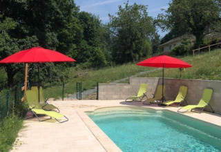Outdoor pool at Domaine Le Faulion with red umbrellas, green lounge chairs, and lush greenery around.