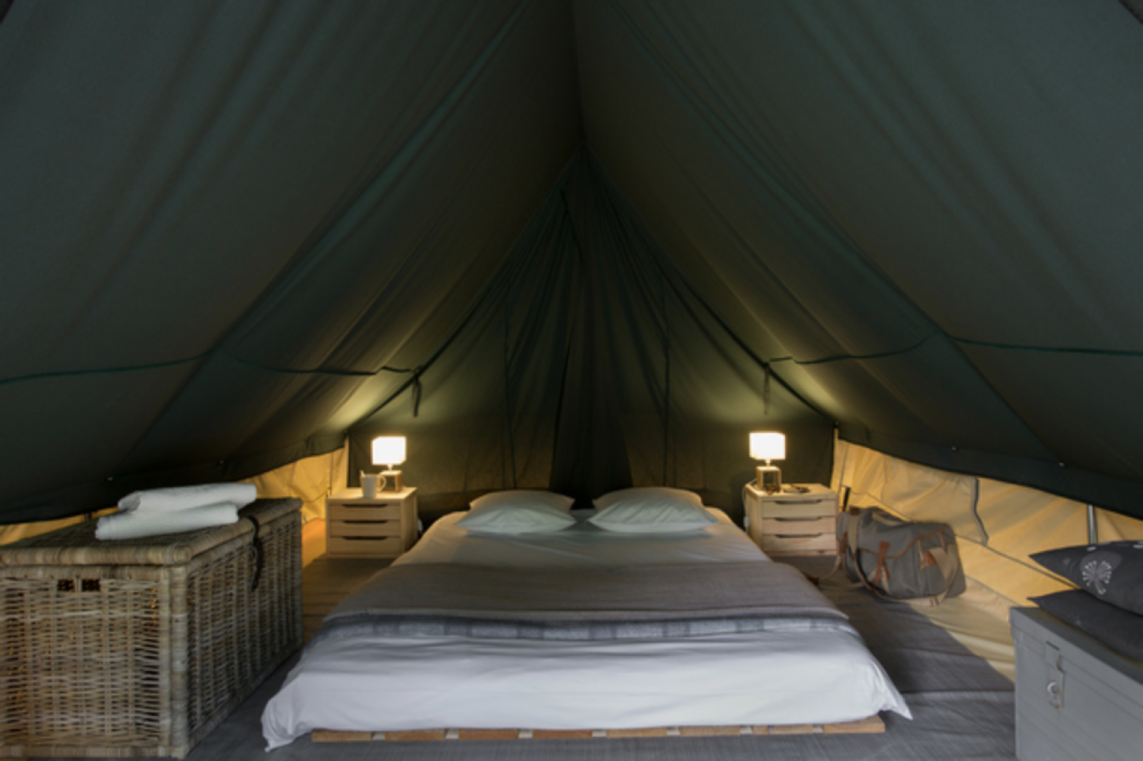Interieur van een safaritent bij Huttopia Champagny met tweepersoonsbed, lampjes en opbergmanden.