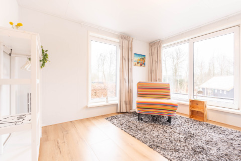 Stanza luminosa a Villa «BushBush» a De Kremmer, Paesi Bassi, con sedia colorata e ampie finestre.