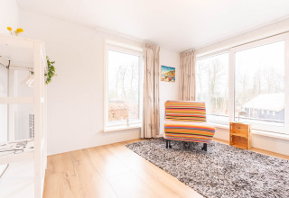 Stanza luminosa a Villa «BushBush» a De Kremmer, Paesi Bassi, con sedia colorata e ampie finestre.