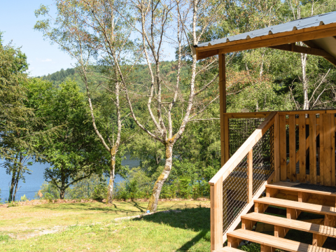 Vista desde la VIP Premium Lodge en Flower Camping La Plage, Francia, con terraza de madera, árboles y lago.