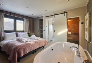 Schlafzimmer in der Happy Oak Wellnesslodge mit Doppelbett, freistehender Badewanne und Sauna.