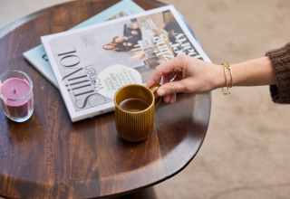 Eine Hand greift nach einer Kaffeetasse auf einem Tisch mit Zeitschriften im Happy Oak wellnesslodge.