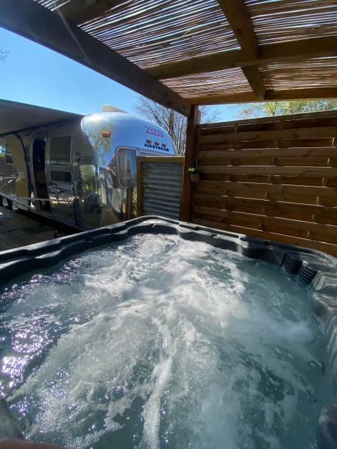 Udsigt over en boblende jacuzzi og en amerikansk Airstream-campingvogn på Campsite Le Château i Frankrig.
