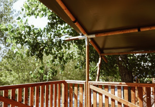 Terrazza in legno con recinzione e copertura in tela al Safari tent al Campeggio Saint Amand, Francia, tra alberi.