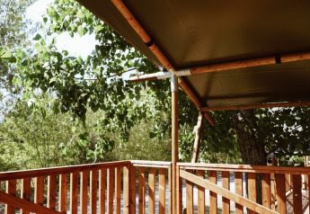 Wooden deck with fence and canvas roof at the Safari tent, Campsite Saint Amand, France, surrounded by trees.