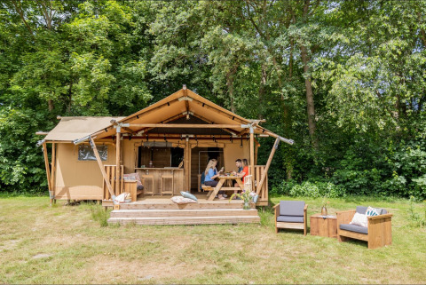 Safari-Zelt Dreamer 40 mit Holzterrasse im Grünen, Menschen am Tisch, gemütliche Sitzmöbel draußen.