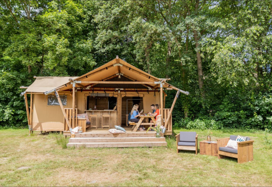 Safari-Zelt Dreamer 40 mit Holzterrasse im Grünen, Menschen am Tisch, gemütliche Sitzmöbel draußen.