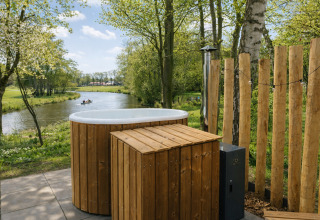 Buiten bubbelbad met houten omkasting bij de rivier en bos aan River Mirrorlodge, Mölke, Nederland.