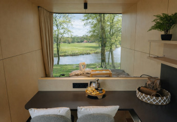 Vista desde River Mirrorlodge en Holiday park Mölke, Países Bajos, de un río y vegetación tras una ventana.