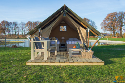 Safari telt med træterrasse, havemøbler og udsigt over sø og natur, ideelt til afslappet glamping.