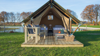 Safari-Zelt mit Holzterrasse, Sitzmöbeln und Blick auf einen Teich in einer natürlichen Umgebung.