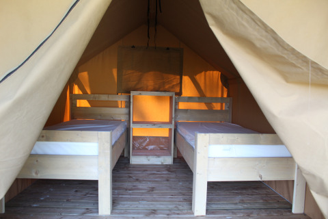 Interno di una tenda safari con due letti singoli e pavimento in legno, perfetta per una vacanza all’aperto.