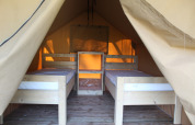 Vista interior de una tienda safari con dos camas individuales y suelo de madera para una experiencia cómoda.