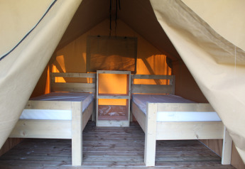Interior view of a safari tent featuring two single beds and a wooden floor, perfect for a camping trip.
