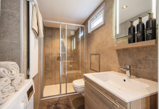 Modern bathroom at Marina Lemmer holiday park, Friesland, with shower, sink, mirror, and washing machine.