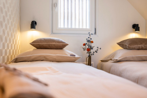 Two cozy single beds with beige linens at Marina Lemmer holiday park in Friesland, Netherlands, with a vase.