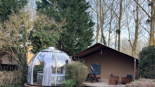 Woody Safari Tent met jacuzzi in een doorzichtige koepel, omgeven door bomen en houten veranda.