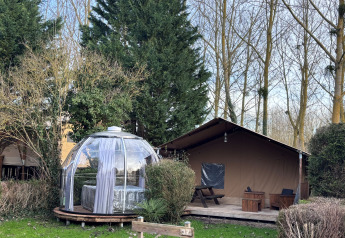 Woody Safari Tent met jacuzzi in glazen koepel, gesitueerd naast houten terras, omgeven door bomen.