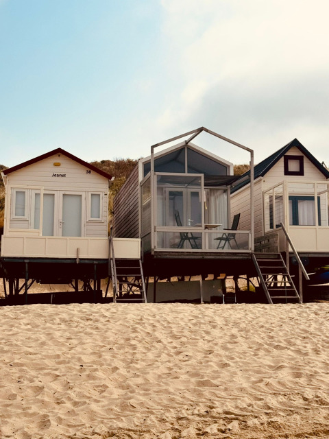 Drei kleine Strandhäuser, darunter Beach sleep house Dishoek 37, auf Sandstrand bei sonnigem Himmel.