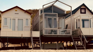 Tres pequeñas casas de playa, incluida Beach sleep house Dishoek 37, sobre la arena bajo un cielo soleado.