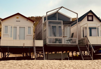 Trois petites maisons de plage, dont Beach sleep house Dishoek 37, sur le sable sous un ciel ensoleillé.