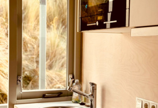 Modernes Mini-Küchenbereich im Beach sleep house «Dishoek 37» mit Fenster und Spüle, Zeeland, Niederlande.