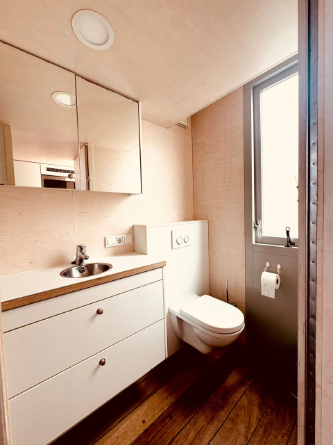 Baño moderno con inodoro flotante, lavabo, armarios con espejo y suelo de madera en Beach sleep house Dishoek, Países Bajos.