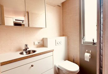 Modernes Badezimmer mit schwebender Toilette, Spiegel, Waschbecken und Holzfußboden im Beach sleep house Dishoek.