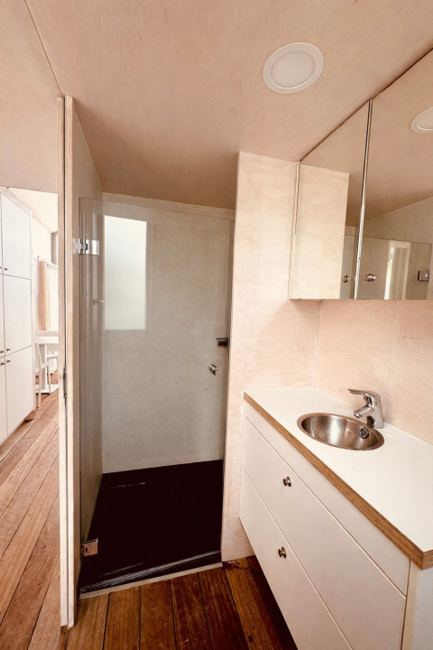 Modern bathroom in a tiny house featuring wooden floor, shower stall and sink at Beach sleep house Dishoek 37.