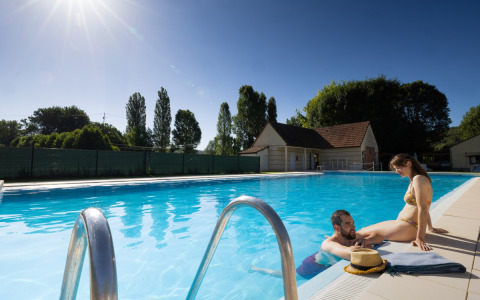 Due persone si rilassano a bordo piscina al campeggio Le Moulin de Bel Air in Occitania, Francia in una giornata soleggiata.