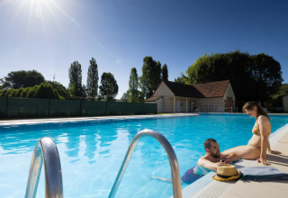 Two people relaxing by the pool at Campsite Le Moulin de Bel Air in Occitanie, France on a sunny day.