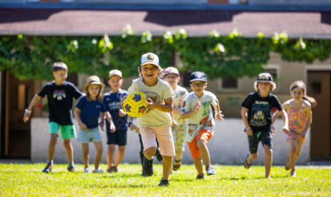 Children playing soccer on a sunny lawn at Campsite Le Moulin de Bel Air holiday park in Occitanie, France.