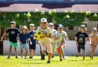 Children playing soccer on a sunny lawn at Campsite Le Moulin de Bel Air holiday park in Occitanie, France.