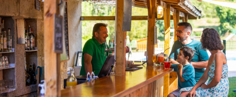Famiglia beve e conversa con il barista al bar all’aperto al campeggio Le Moulin de Bel Air in Occitania, Francia