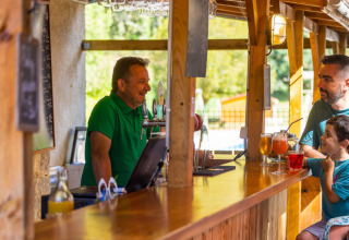 Famiglia beve e conversa con il barista al bar all’aperto al campeggio Le Moulin de Bel Air in Occitania, Francia
