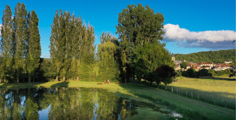 Vista suggestiva di uno stagno, alberi e villaggio dal campeggio Le Moulin de Bel Air in Occitania, Francia.
