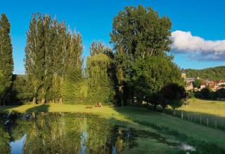 Vista suggestiva di uno stagno, alberi e villaggio dal campeggio Le Moulin de Bel Air in Occitania, Francia.