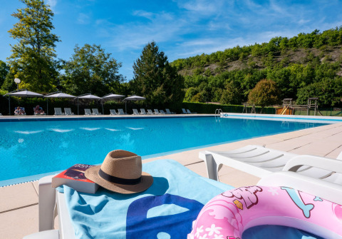 Outdoor pool at Campsite Le Moulin de Bel Air in Occitanie, France, with sun loungers and green hills.