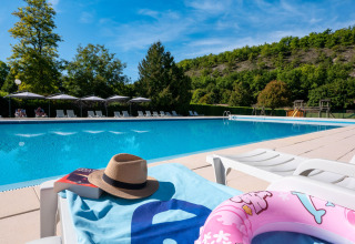 Piscina del campeggio Le Moulin de Bel Air in Occitania, Francia, con sdraio e colline verdi sullo sfondo.
