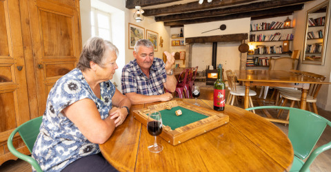 Coppia anziana gioca a un gioco da tavolo con vino a Le Moulin de Bel Air, campeggio in Occitania, Francia.